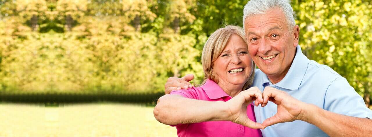 Two senior citizens making a heart with their hands.