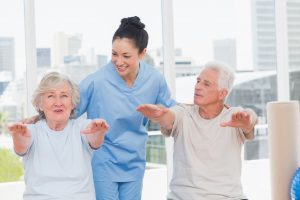 Two seniors seated performed arm exercised with a female caregiver.