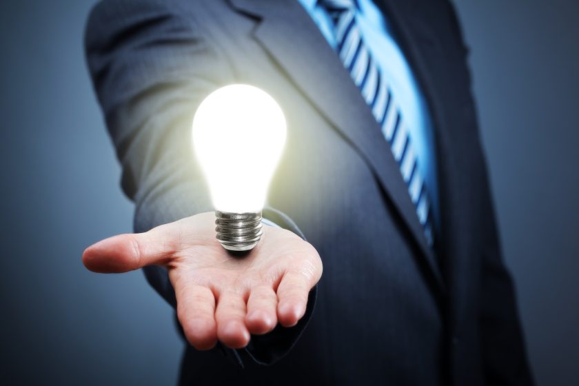 A man in a suit with his hand outstretched, in the hand is a lit lightbulb.