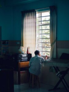 old man looking out window of dark room