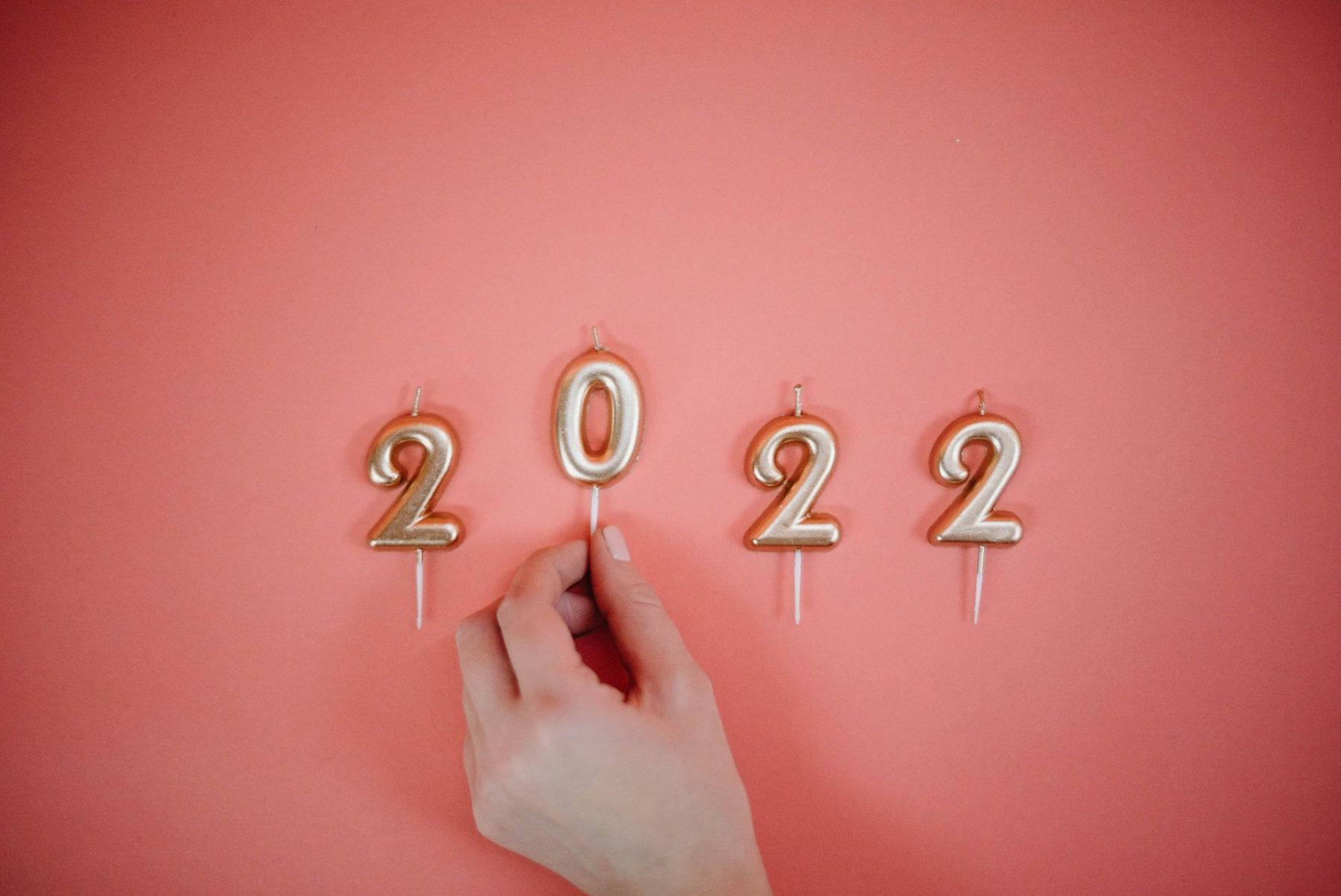 hand placing 2022 gold candles on pink background