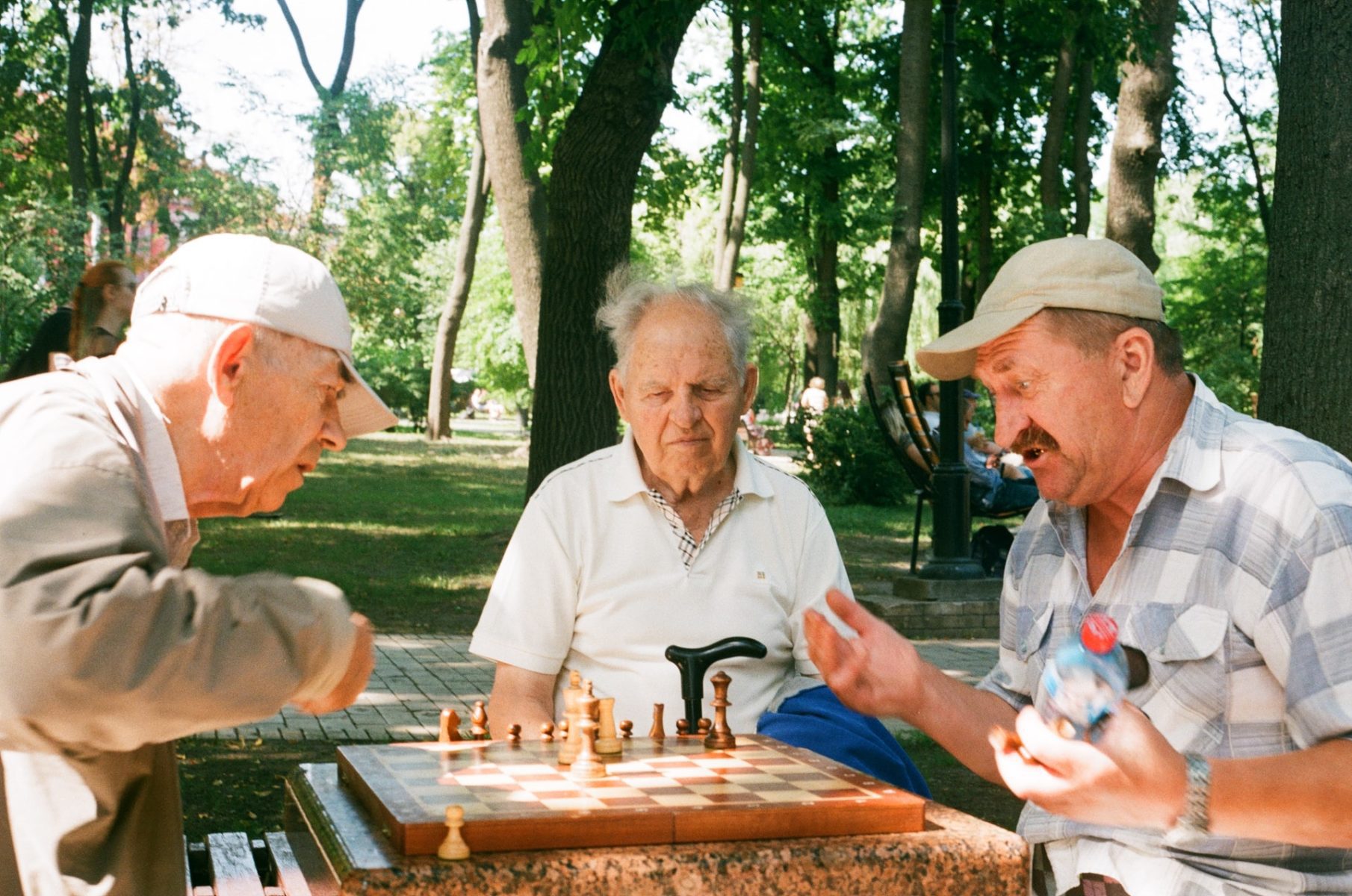 A group of three senior age friends playing chess in the park