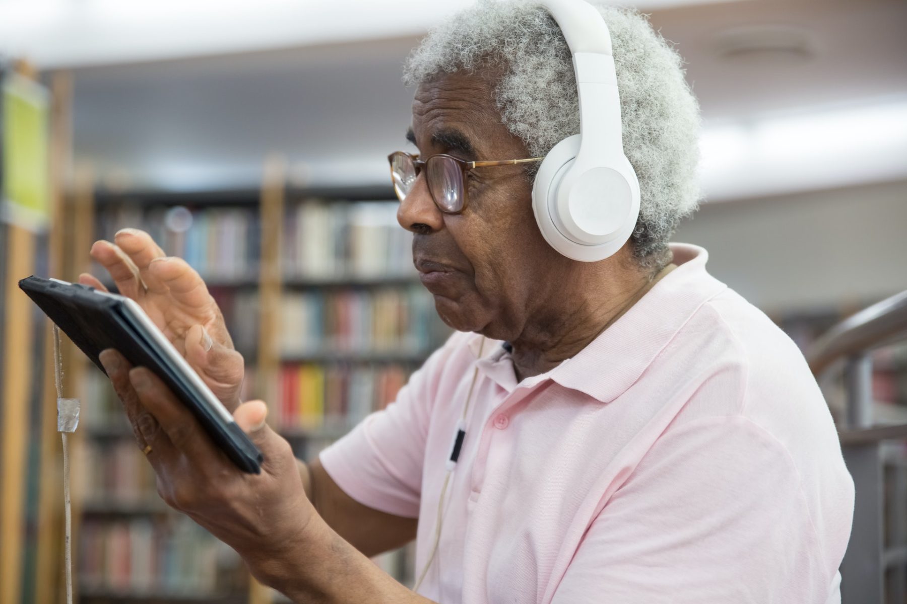 An elderly man stays cool listening to music at the library.