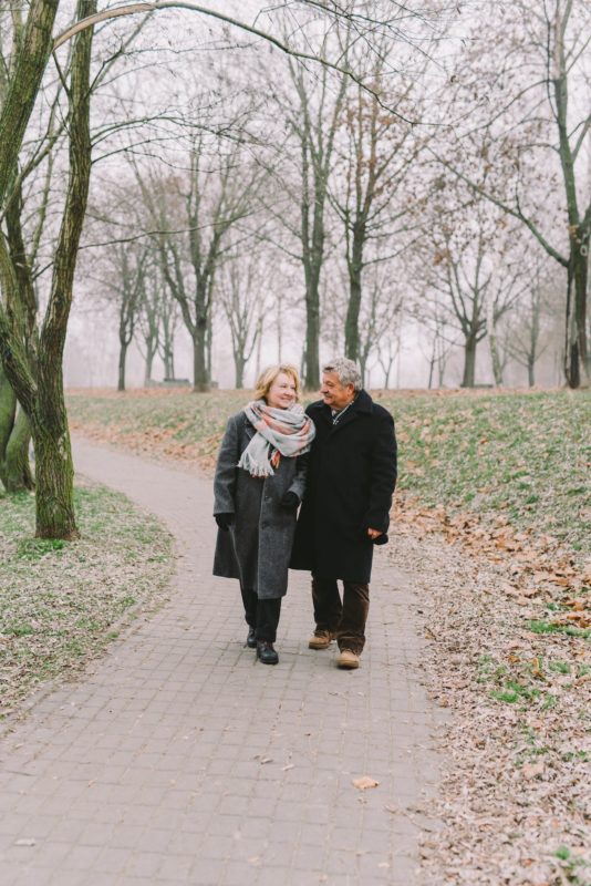 Two seniors walk in a park during winter.