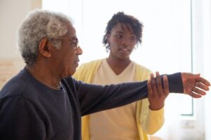 A caregiver helps an elderly client with rehab exercises after surgery.