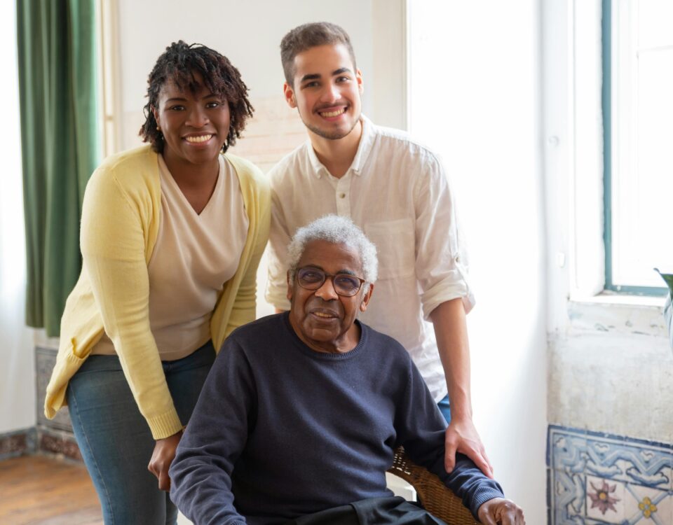 An adult child, their elderly parent, and a professional caregiver pose for a photo.