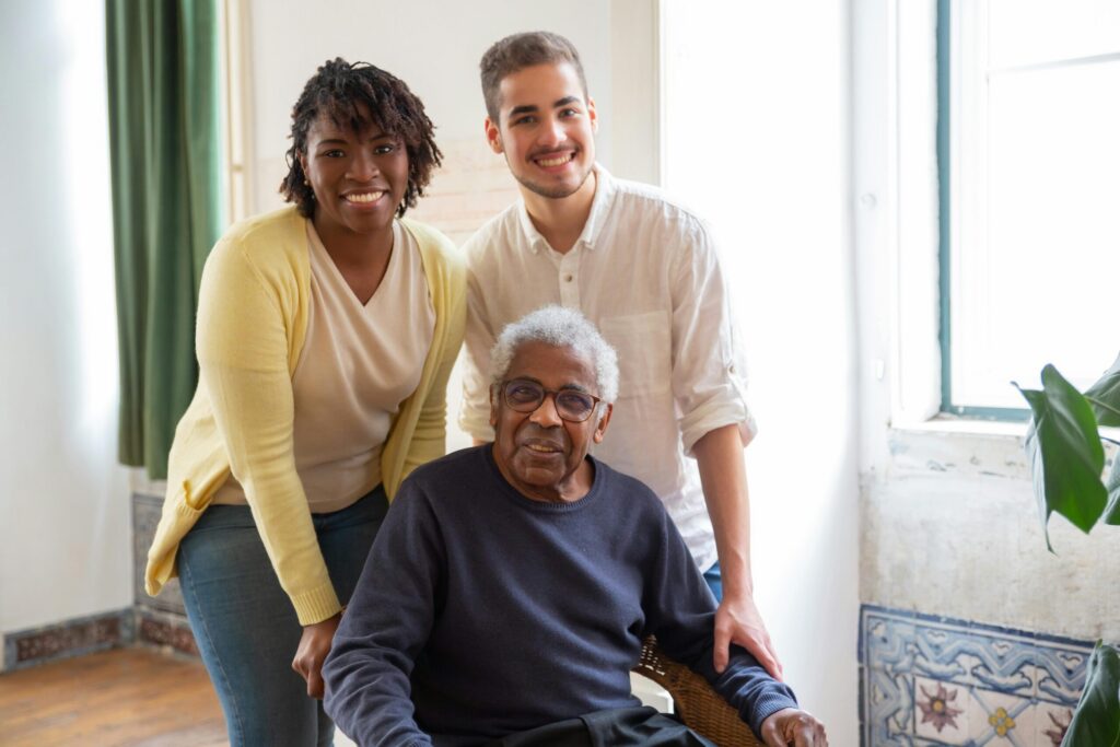 An adult child, their elderly parent, and a professional caregiver pose for a photo.