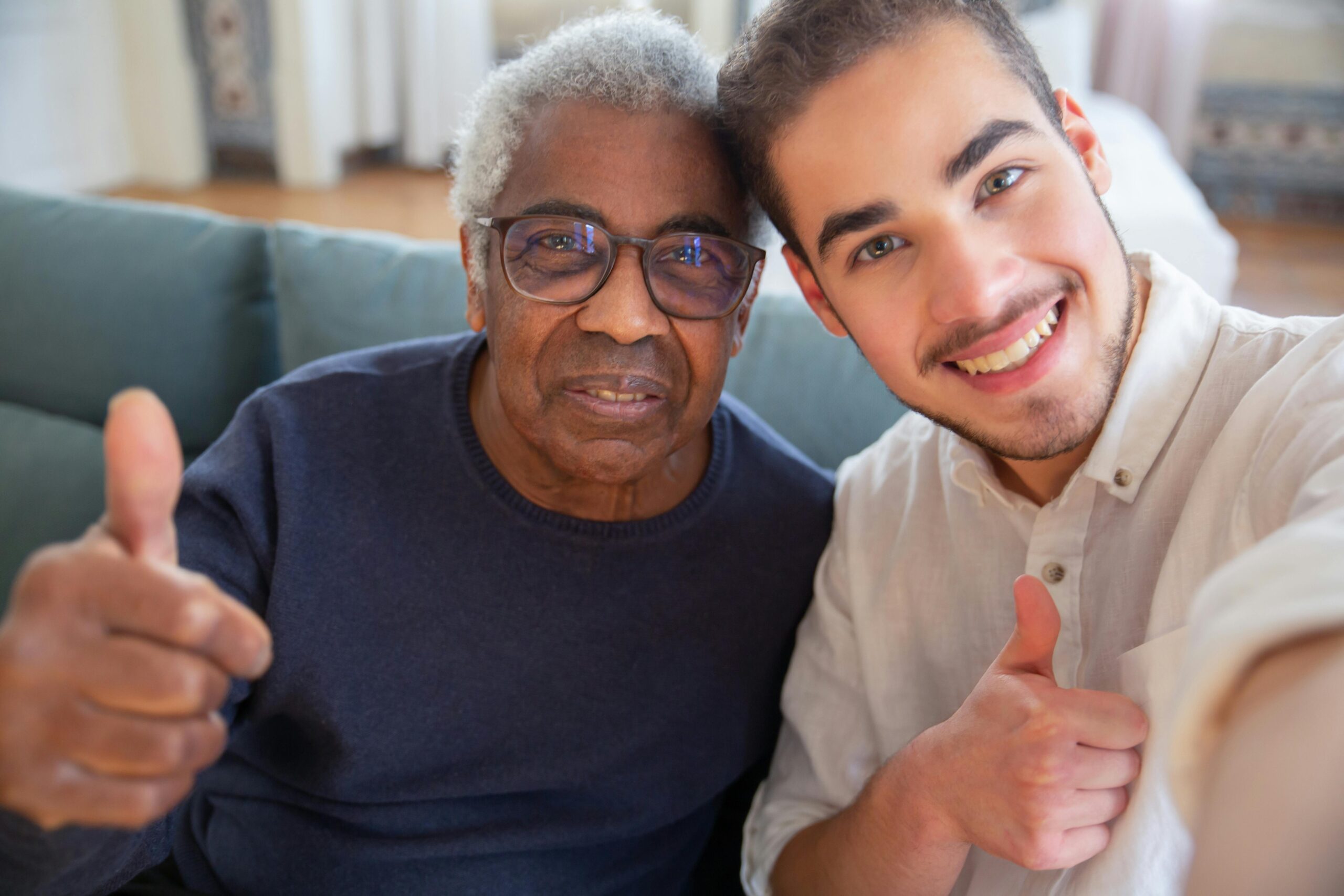 An elderly man and his caregiver pose for a photo giving the thumbs-up sign